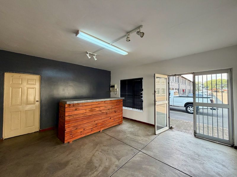 Commercial office space featuring a built-in wooden service counter, concrete flooring, security gate access, and a combination of fluorescent and track lighting.