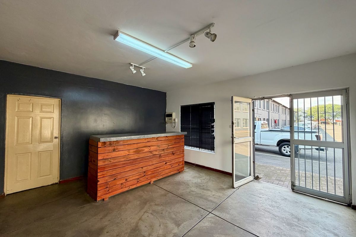 Commercial office space featuring a built-in wooden service counter, concrete flooring, security gate access, and a combination of fluorescent and track lighting.