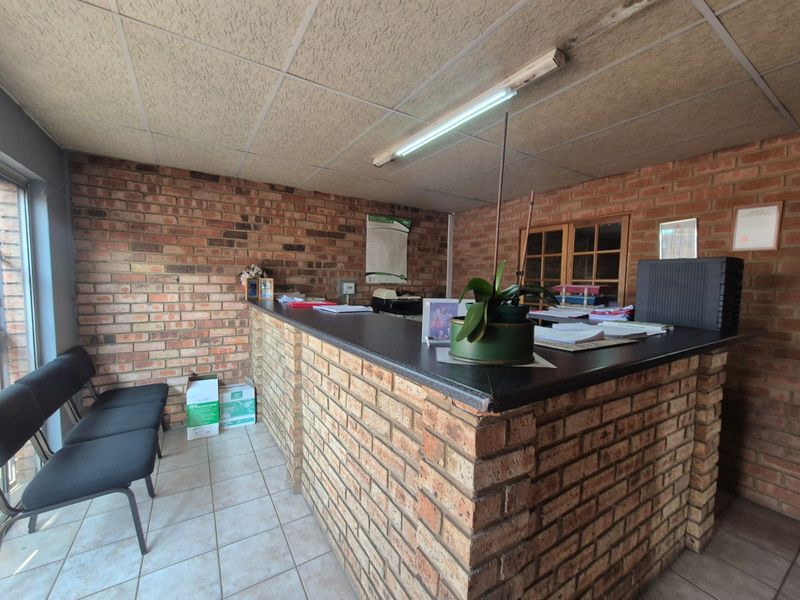 Office reception area featuring a built-in brick counter, exposed brick walls, and tiled flooring, providing a functional workspace environment.