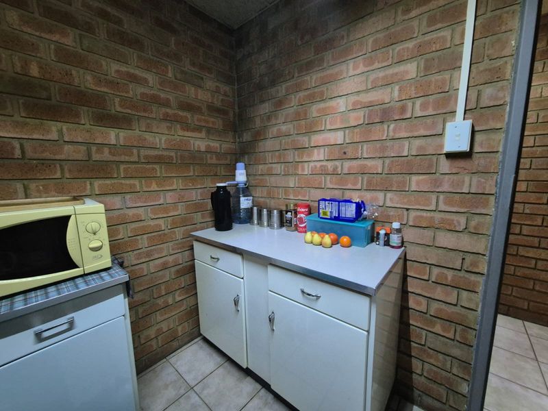 A compact office kitchenette featuring exposed brick walls, laminate countertops, and functional built-in cabinetry.