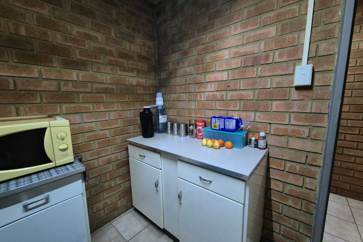 A compact office kitchenette featuring exposed brick walls, laminate countertops, and functional built-in cabinetry.