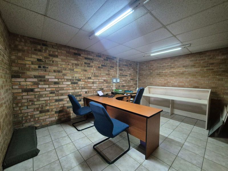 Functional office space featuring exposed brick walls, ceramic tile flooring, suspended ceiling, and a built-in reception counter.