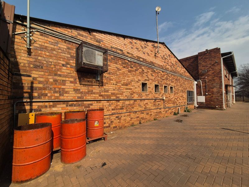 Rear exterior view of the office building featuring a face brick facade, paved courtyard area, and wall-mounted HVAC unit.