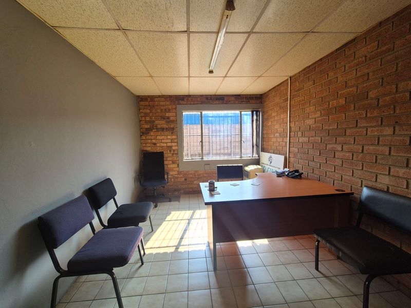 A functional office space featuring exposed brick walls, ceramic tiled flooring, and a suspended ceiling with integrated lighting.