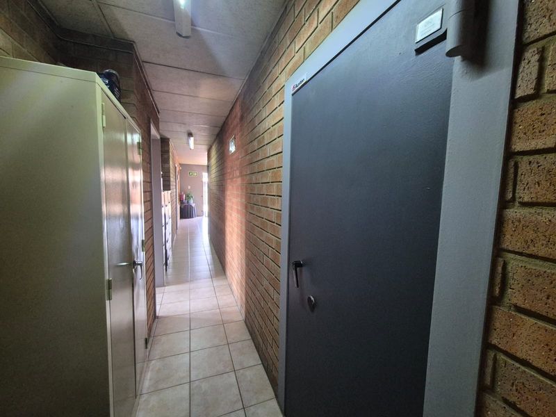 A functional office hallway featuring exposed brick walls, tiled flooring, and a suspended ceiling with integrated lighting.