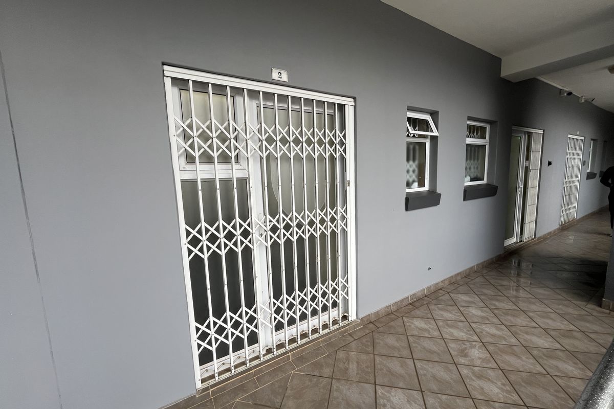 Exterior view of an office entrance featuring a secure metal gate, tiled walkway, and modern grey painted facade.