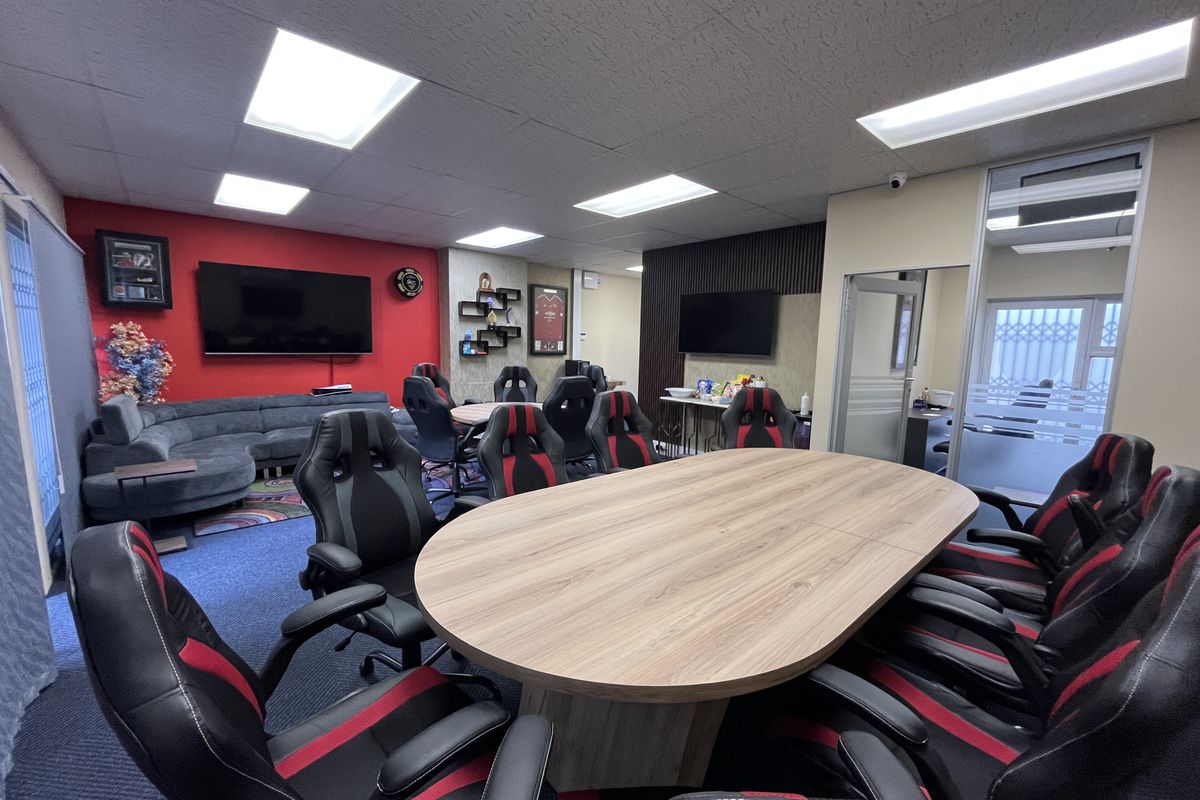 A modern office space featuring a large meeting table, glass partitioning, slatted wall accents, and recessed ceiling lighting.