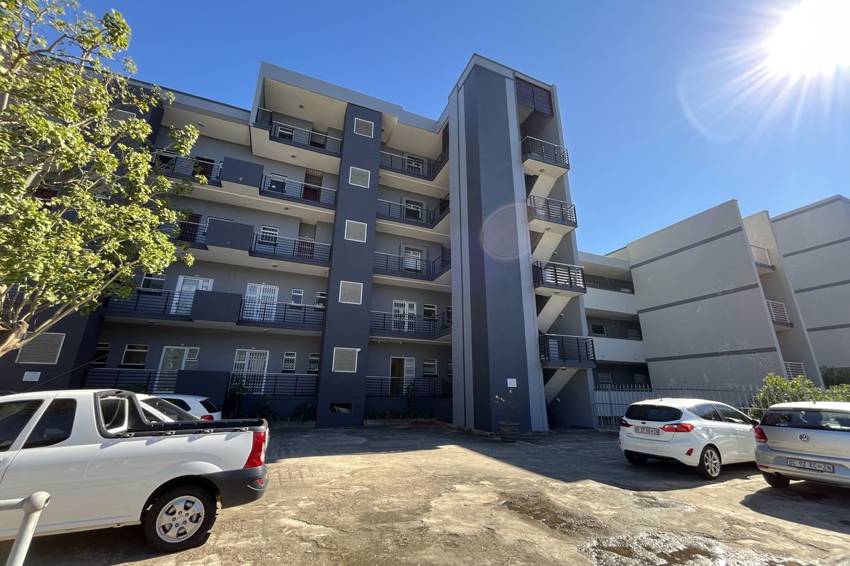Exterior view of a multi-story office building featuring balconies, an external stairwell, and a paved parking area.