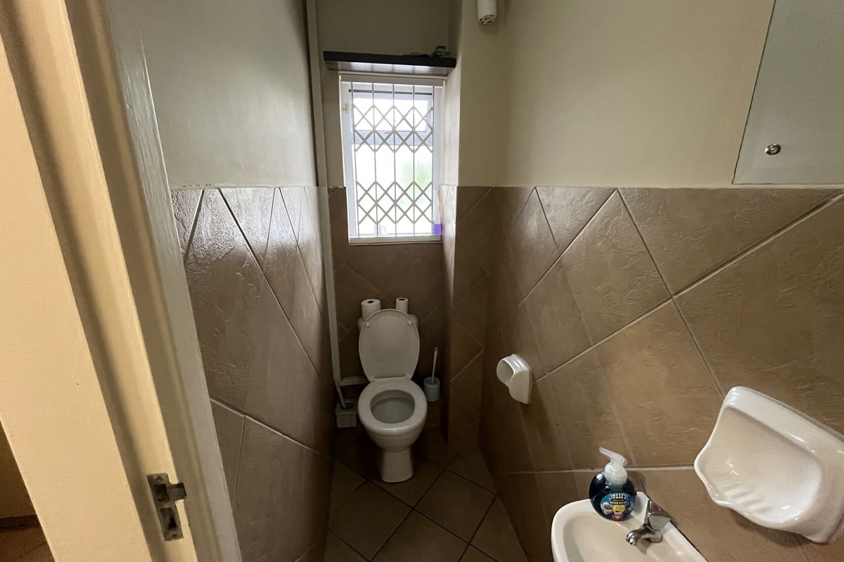 A compact bathroom featuring a toilet, wall-mounted basin, and tiled finishes with a security-gated window.