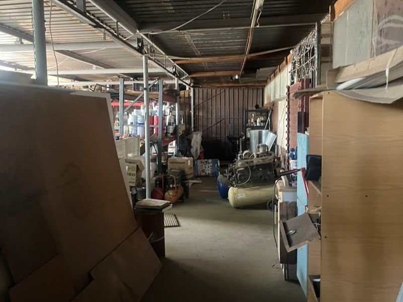 Industrial utility space featuring a corrugated metal roof, exposed steel structural beams, and concrete flooring, suitable for storage or workshop use.