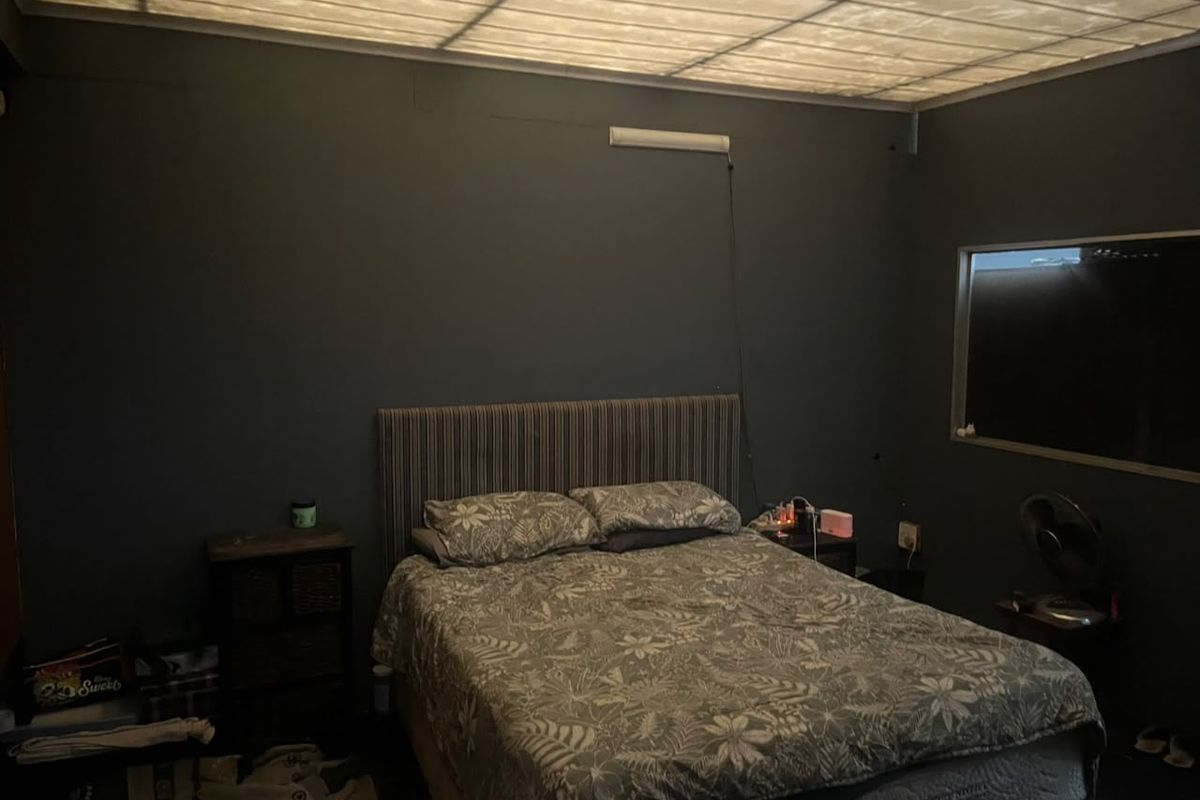 A bedroom featuring dark painted walls, a suspended ceiling panel, and a fixed window. The space requires cosmetic updates to improve overall appeal.
