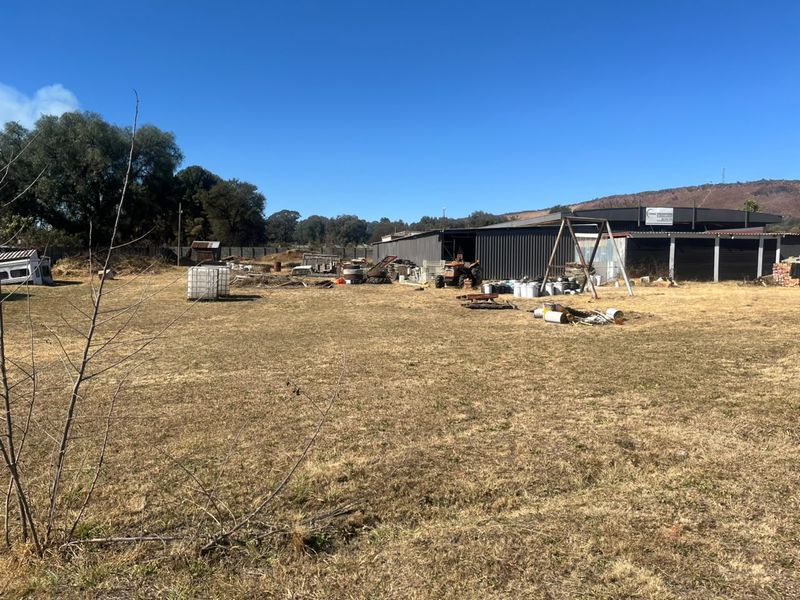 Expansive industrial yard area featuring a large corrugated metal shed structure and perimeter fencing, suitable for storage or operational use.