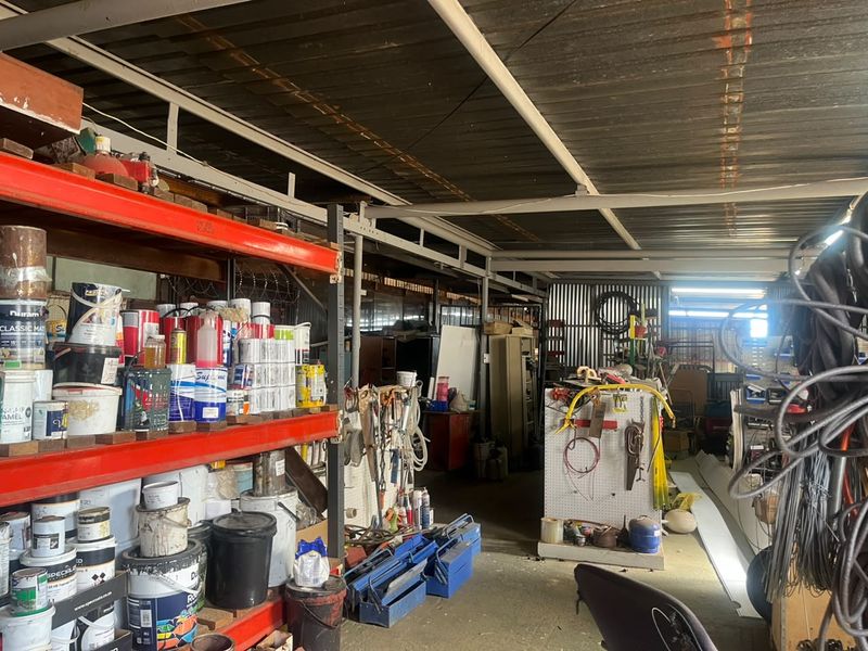 Industrial utility space featuring exposed steel roof structure, heavy-duty metal shelving units, and pegboard storage systems for equipment and supplies.