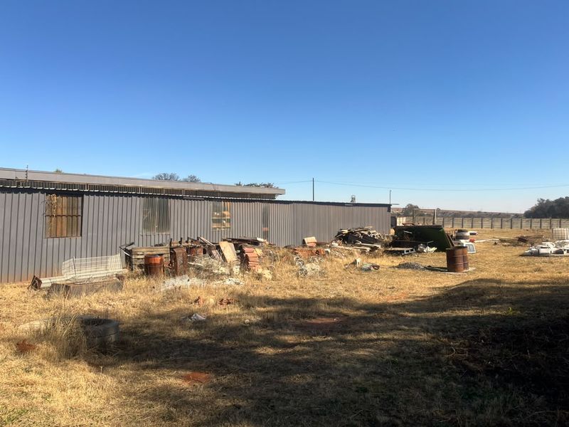 Rear view of an industrial building featuring corrugated metal cladding and security bars, set within a large, unmaintained yard area.