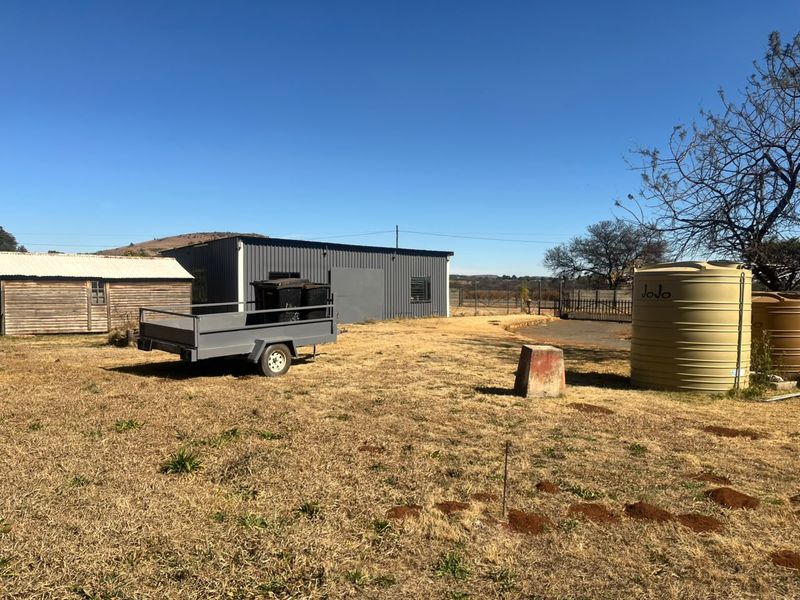 Exterior view of the industrial property featuring a corrugated metal workshop, a timber shed, and water storage tanks on a large open plot.
