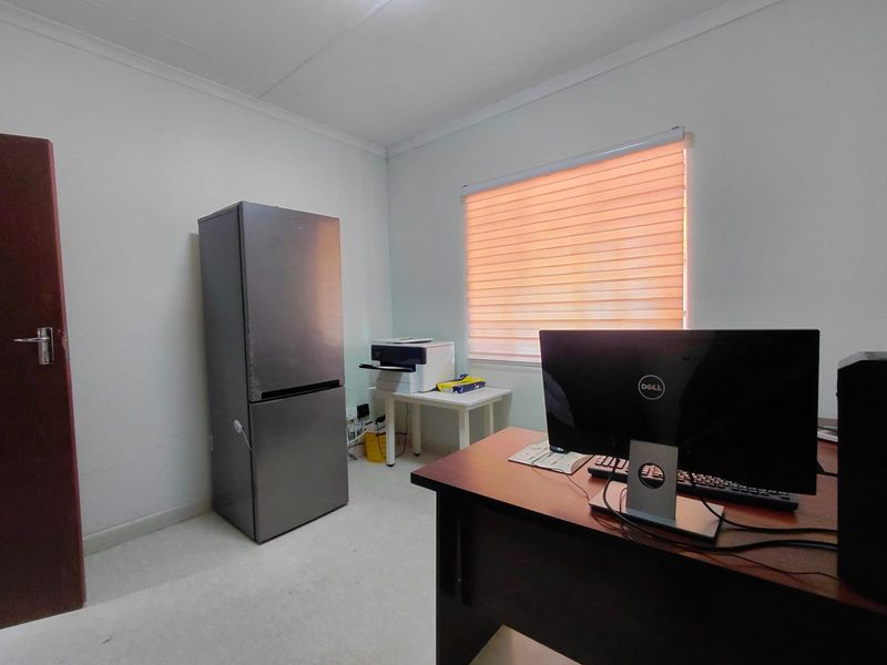 A functional office space featuring neutral walls, a window with a roller blind, and standard electrical infrastructure.