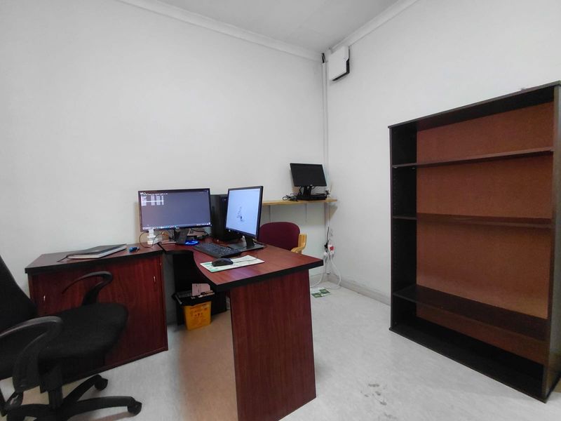 A functional office space featuring plain white walls, vinyl flooring, and surface-mounted electrical infrastructure.