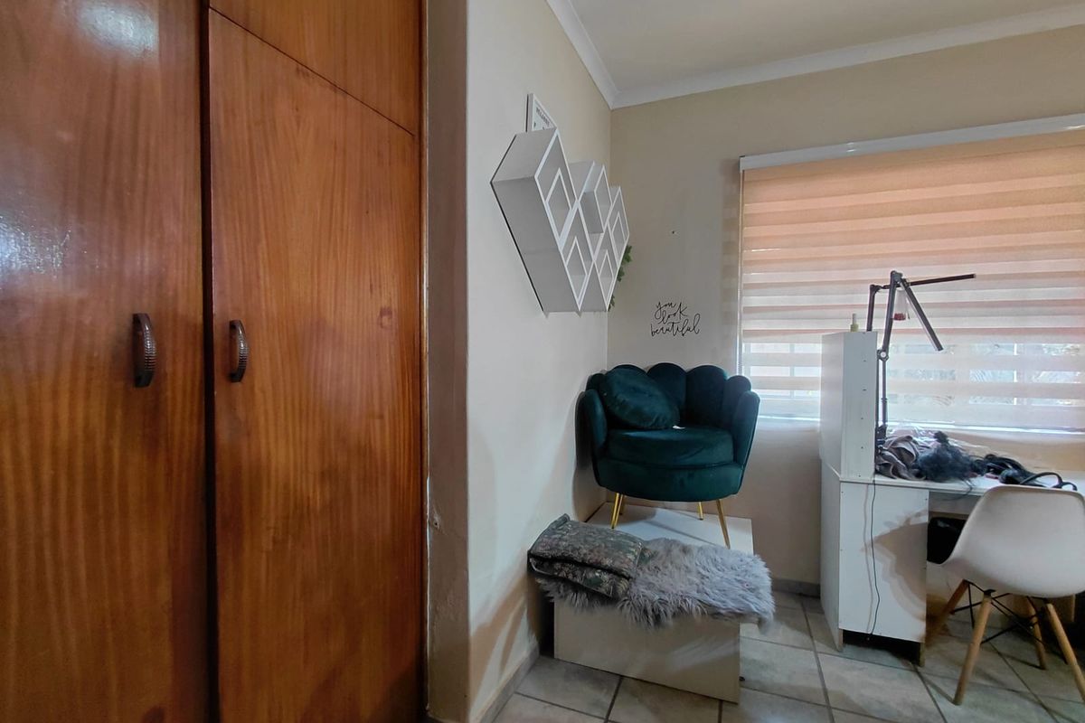 A bedroom featuring built-in wooden cupboards, tiled flooring, and a window fitted with roller blinds.