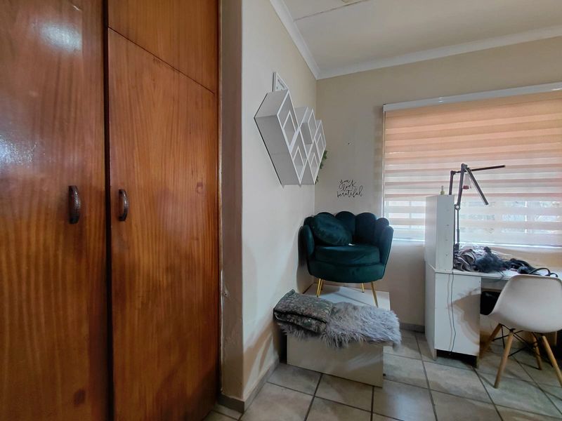 A bedroom featuring built-in wooden cupboards, tiled flooring, and a window fitted with roller blinds.