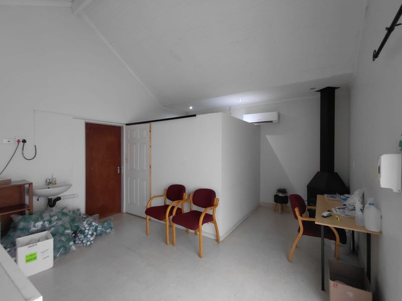 A functional office space featuring a vaulted ceiling, wall-mounted air conditioning, a fireplace, and a convenient wall-mounted basin.