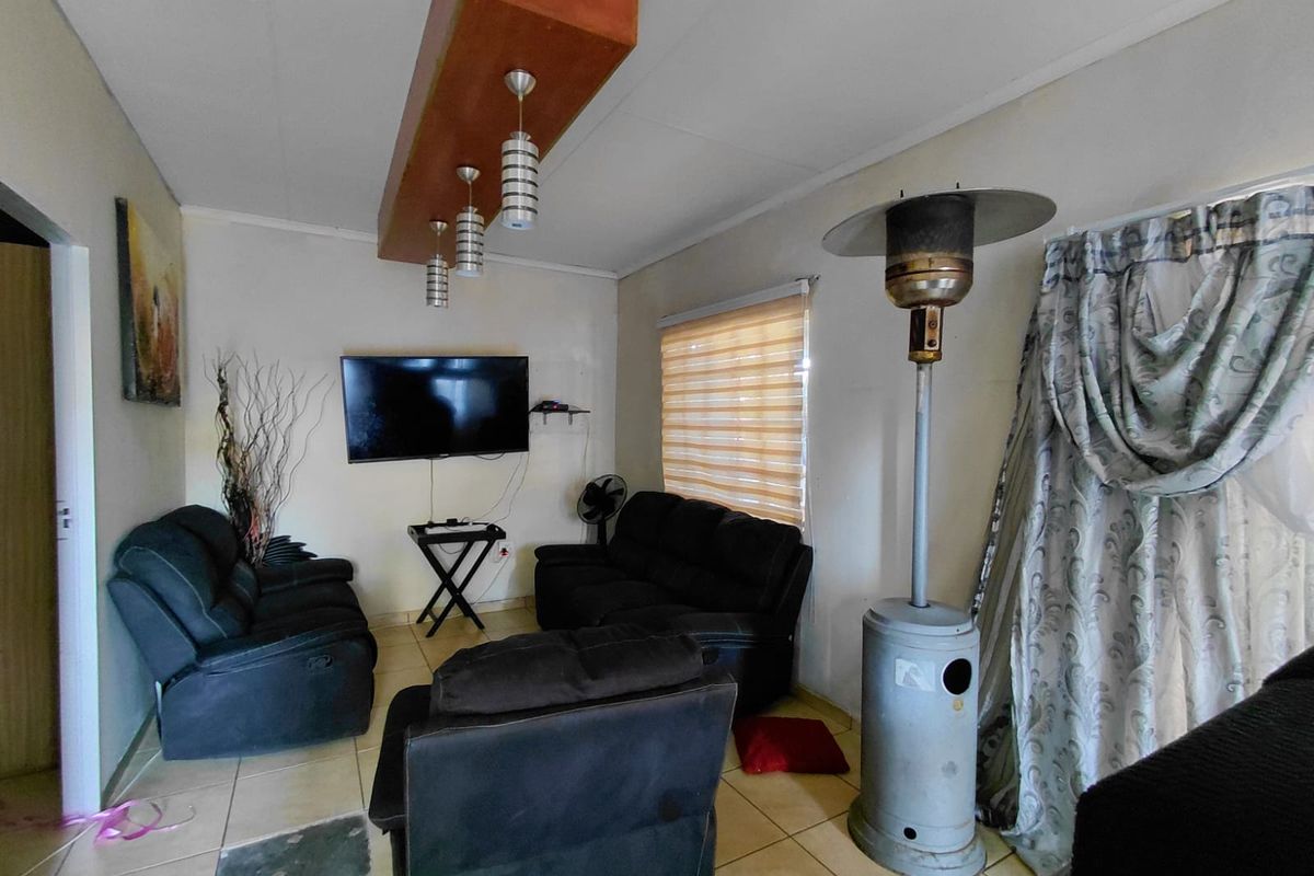 A living room area featuring tiled flooring, a suspended bulkhead lighting fixture, and roller blinds, offering a functional space for commercial or residential use.
