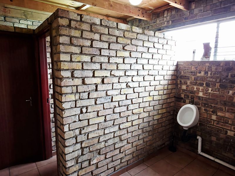 Industrial-style bathroom featuring exposed brick walls, timber ceiling beams, and wall-mounted urinals with tiled flooring.