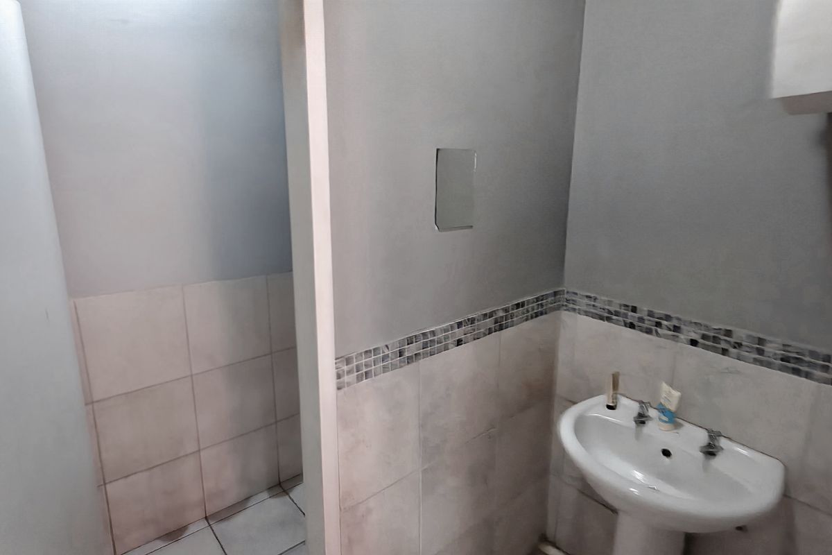 A small industrial-style bathroom featuring a pedestal sink, tiled splashback with mosaic detailing, and neutral wall finishes.