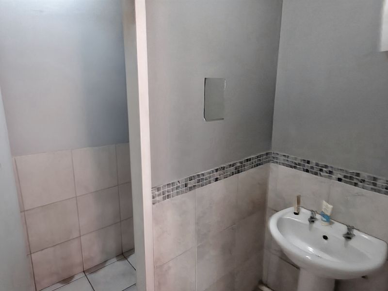 A small industrial-style bathroom featuring a pedestal sink, tiled splashback with mosaic detailing, and neutral wall finishes.
