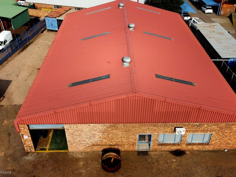 Aerial view of an industrial warehouse featuring a corrugated metal roof with ventilation, brick exterior, and paved yard area.