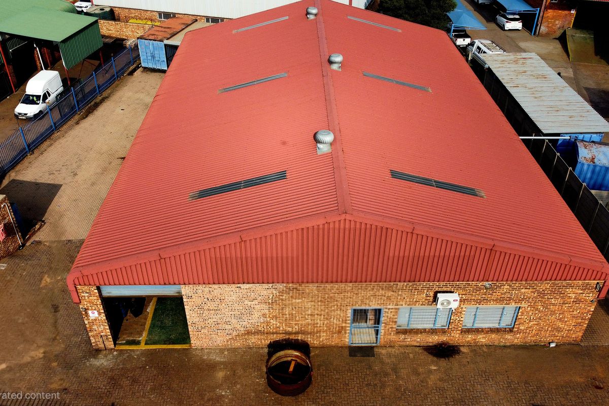 Aerial view of an industrial warehouse featuring a corrugated metal roof with ventilation, brick exterior, and paved yard area.