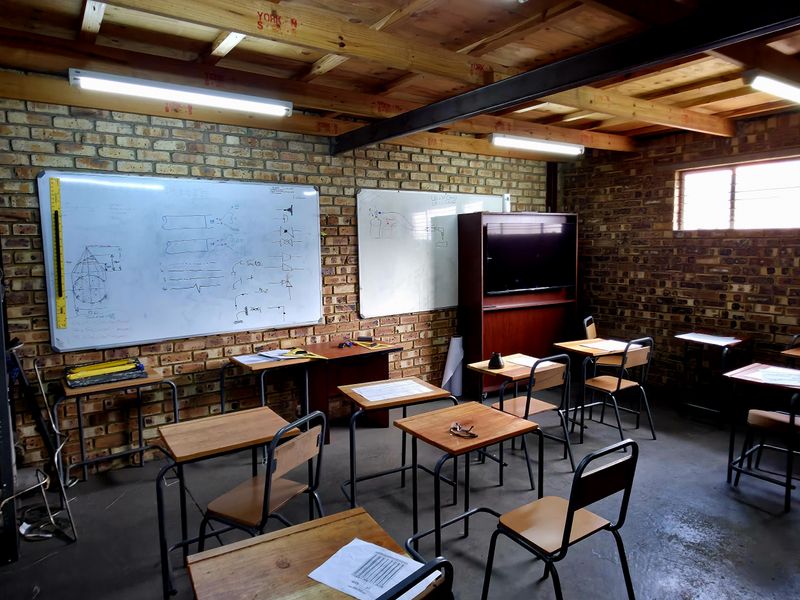 Industrial-style office or training room featuring exposed brick walls, timber beam ceiling, concrete flooring, and wall-mounted whiteboards.
