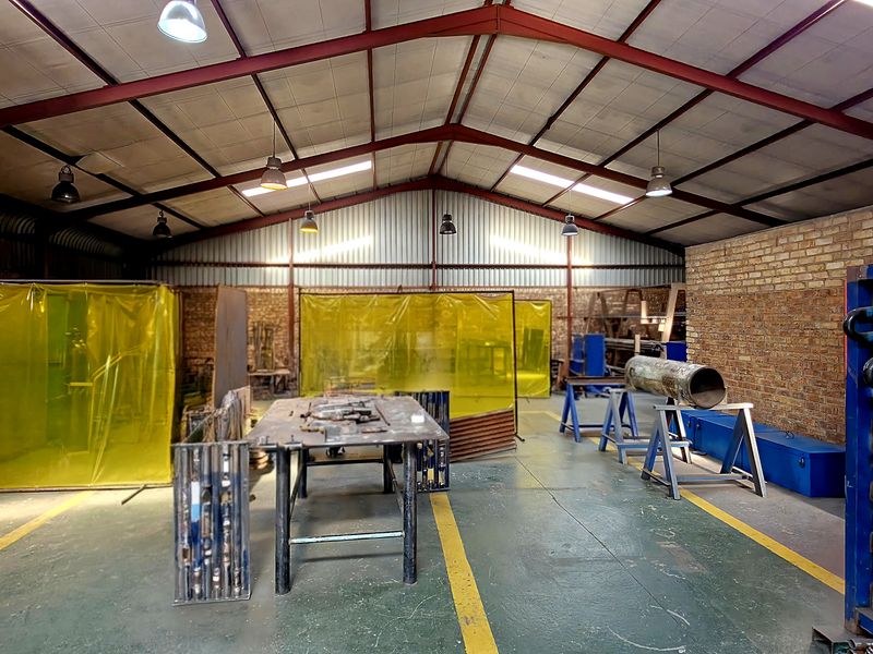 Spacious industrial workshop featuring exposed steel roof trusses, brick walls, and durable painted concrete flooring with designated work zones.