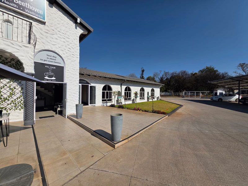 Front exterior view of a retail property featuring a tiled patio, arched windows, and a spacious concrete driveway with covered parking.