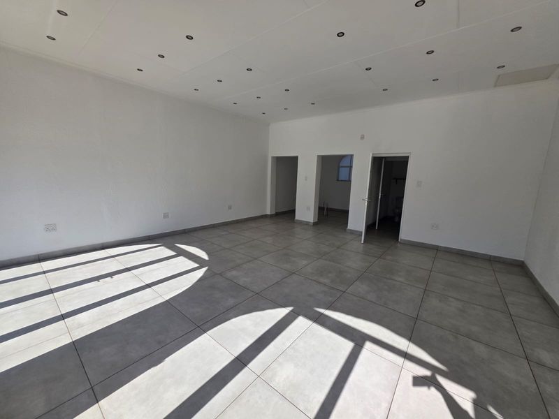 A spacious, empty open-plan retail area featuring neutral tiled flooring and recessed ceiling downlights, offering a versatile layout for various business applications.