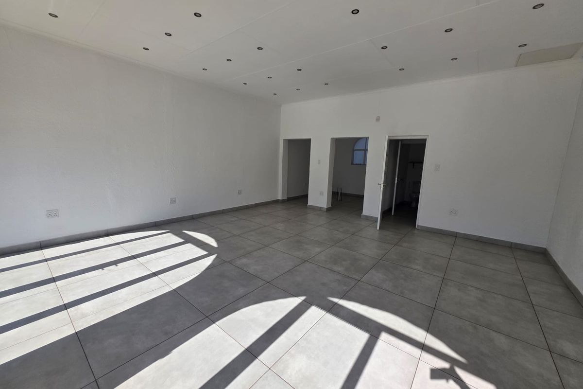 A spacious, empty open-plan retail area featuring neutral tiled flooring and recessed ceiling downlights, offering a versatile layout for various business applications.
