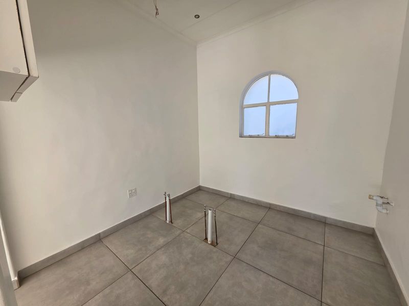 A clean, empty laundry room featuring tiled flooring, an arched window, and dedicated plumbing connections for appliances.