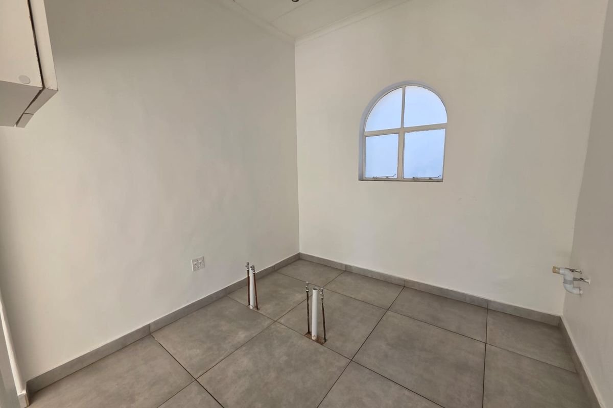 A clean, empty laundry room featuring tiled flooring, an arched window, and dedicated plumbing connections for appliances.