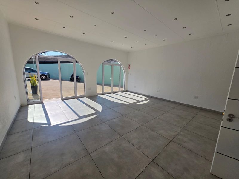 Bright and spacious open-plan retail area featuring large arched glass doors, modern tiled flooring, and recessed ceiling lighting.