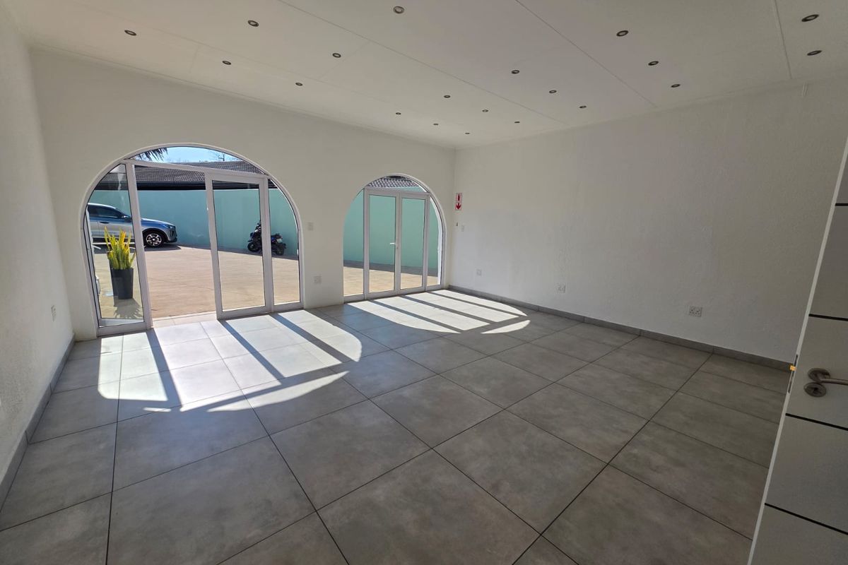 Bright and spacious open-plan retail area featuring large arched glass doors, modern tiled flooring, and recessed ceiling lighting.