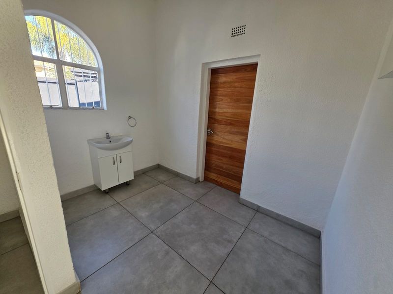 A clean, minimalist bathroom featuring large format floor tiles, a modern vanity with basin, and a distinctive arched window.