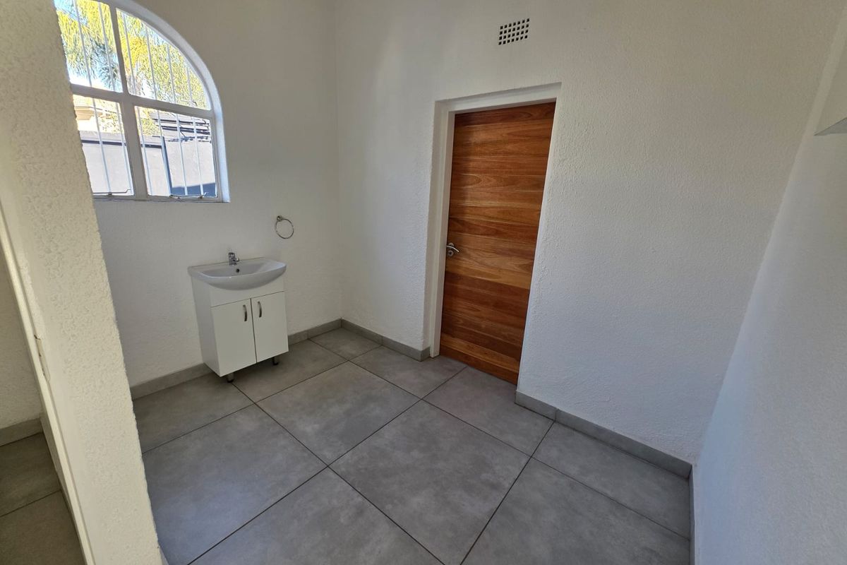 A clean, minimalist bathroom featuring large format floor tiles, a modern vanity with basin, and a distinctive arched window.