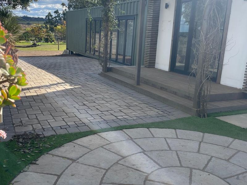 A well-maintained rear exterior area featuring a timber deck, paved patio, and circular stone feature, providing a seamless transition to the office space.