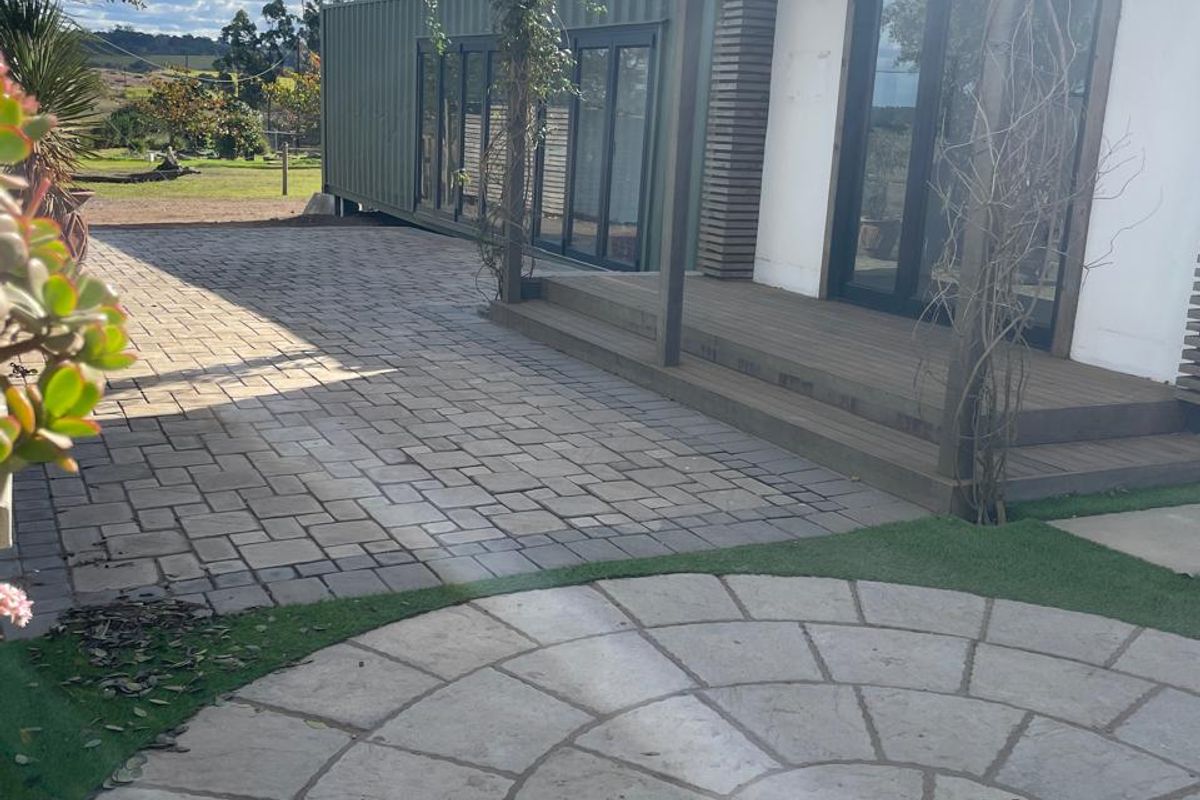 A well-maintained rear exterior area featuring a timber deck, paved patio, and circular stone feature, providing a seamless transition to the office space.