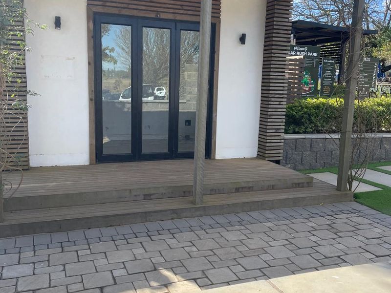 Modern office entrance featuring a timber deck, pergola, and bi-fold glass doors, set against a landscaped stone-paved area.