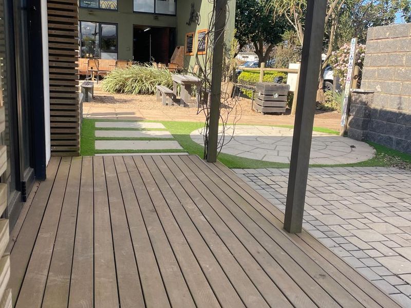 A well-maintained outdoor timber deck leading to a paved courtyard area with a pergola, suitable for office break-out space or outdoor meetings.