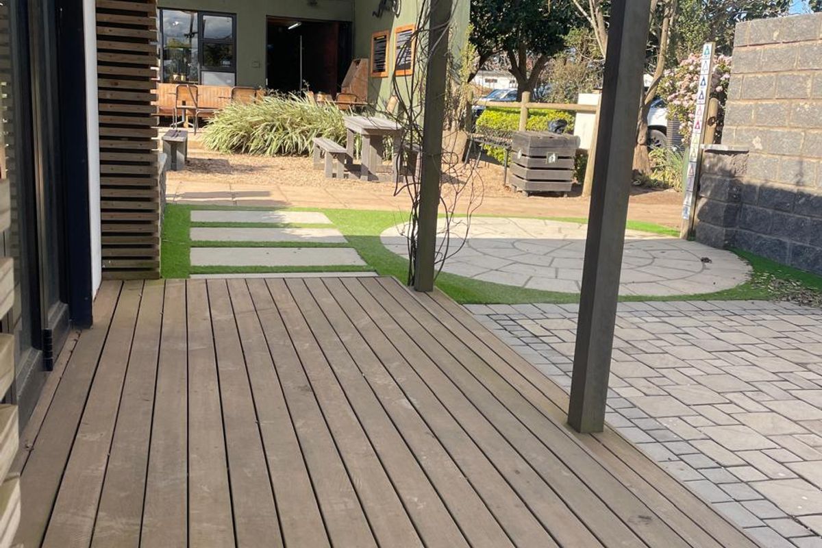 A well-maintained outdoor timber deck leading to a paved courtyard area with a pergola, suitable for office break-out space or outdoor meetings.