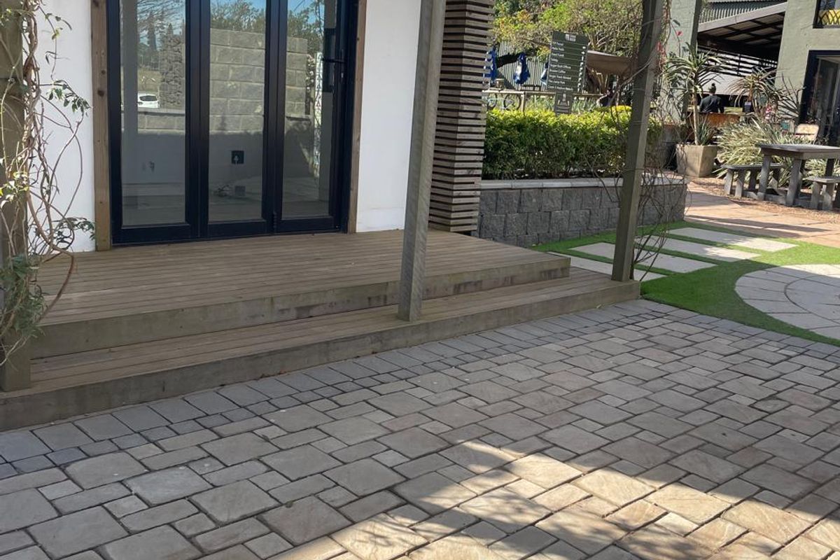 A well-maintained outdoor patio area featuring timber decking, a pergola, and paved flooring, providing a clean and inviting entrance to the office space.