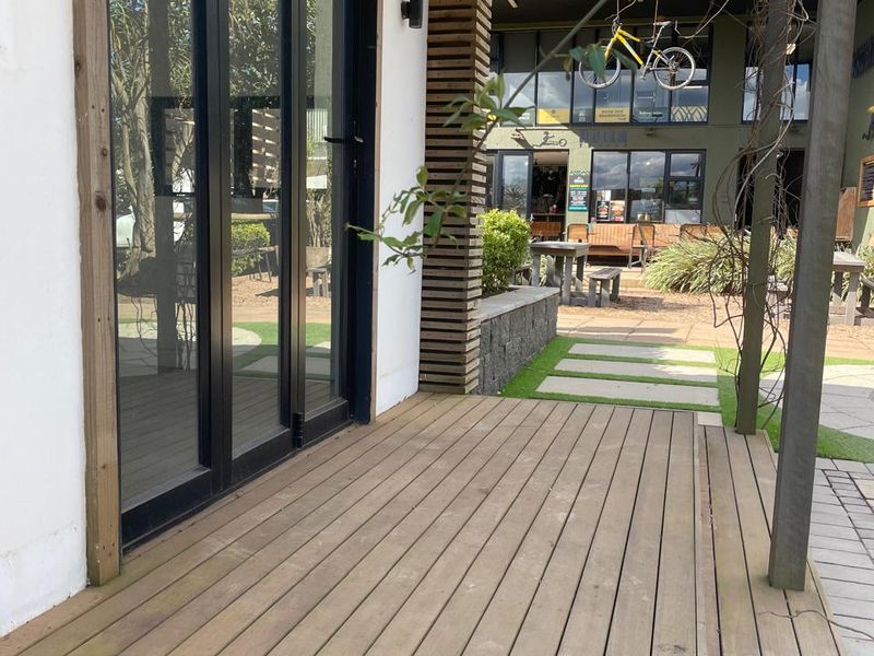 A covered timber deck patio featuring black aluminium glass doors and a timber slat pergola, overlooking an outdoor courtyard area.