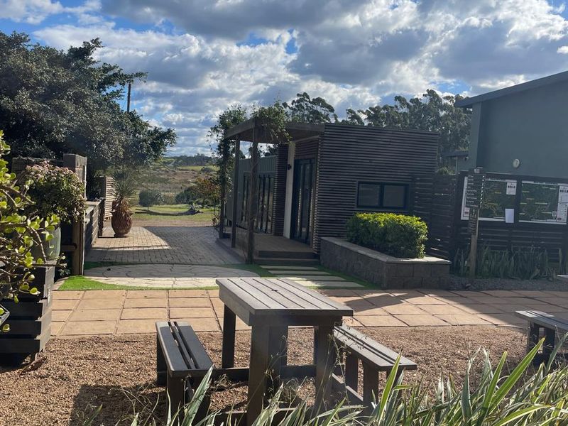 A well-maintained outdoor office area featuring timber-clad structures, paved patio space, and landscaped garden surroundings.