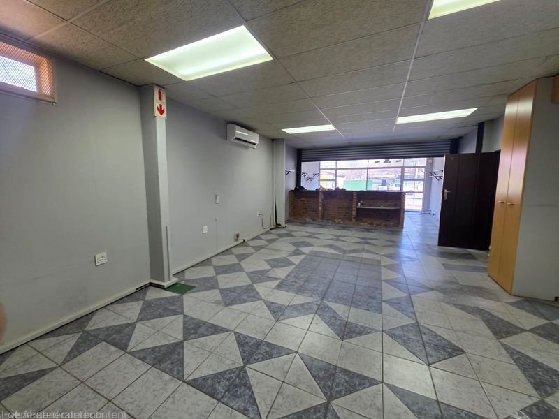 Open-plan retail space featuring tiled flooring, suspended ceiling with recessed lighting, air conditioning, and a built-in brick service counter with security shutter.